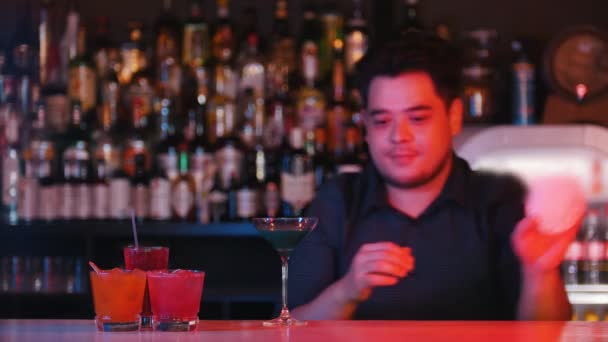 Young professional bartender puts a glass with a blue cocktail on a napkin and gives it forward — Stock Video
