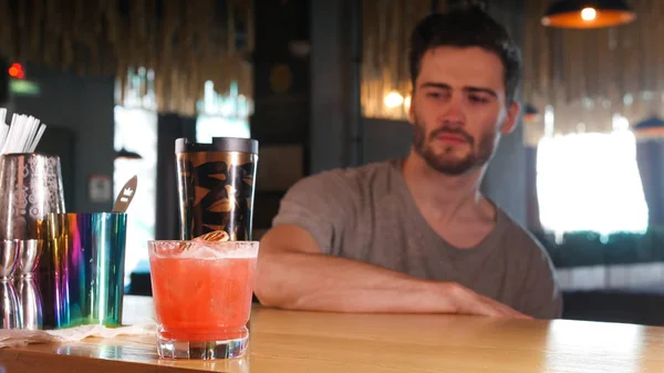 Молодий чоловік сидить біля барної стійки і дивиться на склянку з коктейлем — стокове фото
