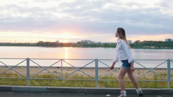 Uma adolescente montando nos patins na orla do rio em um fundo do rio — Vídeo de Stock