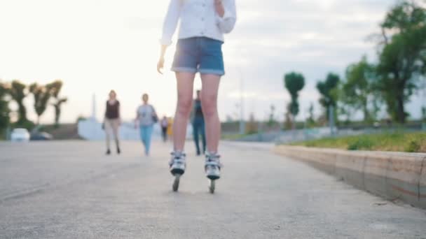 Una adolescente delgada y sonriente en patines patinando en el parque — Vídeo de stock