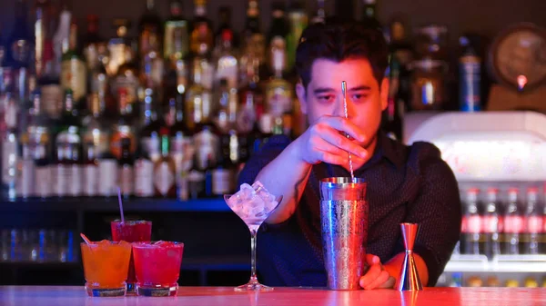 Молодий бармен змішування інгредієнтів в шейкері з ложкою склянка з льодом - коктейлі на підставці — стокове фото