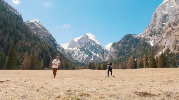 Dois jovens viajantes jogando futebol no campo em um fundo das montanhas e da floresta — Vídeo de Stock