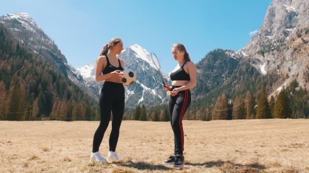 Δύο νεαρές γυναίκες που στέκονται στο γήπεδο-κρατώντας μια ρακέτα και μια μπάλα ποδοσφαίρου-Δολομίτες, Ιταλία — Αρχείο Βίντεο