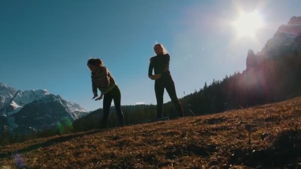 Two young women doing sports outside - bending down - mountains and forest on a background — Stock Video