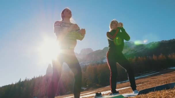 Two young women doing sports outside - squatting - mountains and forest on a background — Stock Video