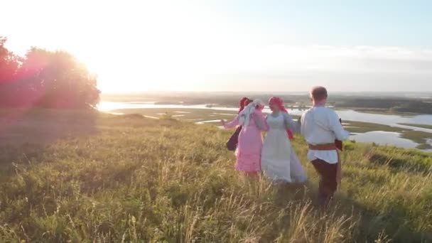 Люди в традиционной русской одежде, стоящие на траве, исполняют танец под музыку балалайки — стоковое видео