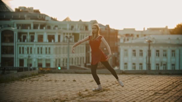 Молодая женщина-балерина тренируется на крыше - стоя на цыпочках и показывая элементы — стоковое видео