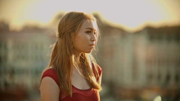 Une jeune femme inspirée en robe rouge debout sur le toit sur un coucher de soleil lumineux — Video