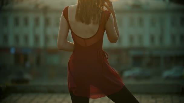 A young graceful woman in red dress standing on the roof and fixing her hair - sunset — Stock Video