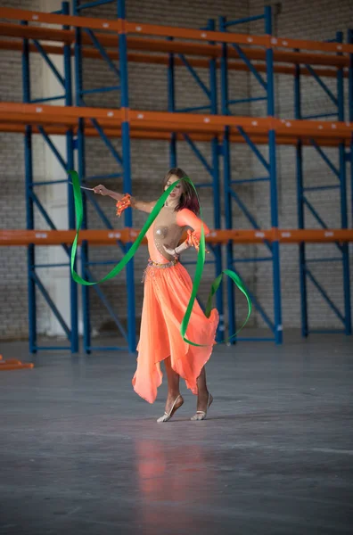 Mujer joven bailando con cinta de gimnasia en las manos en el almacén —  Fotos de Stock