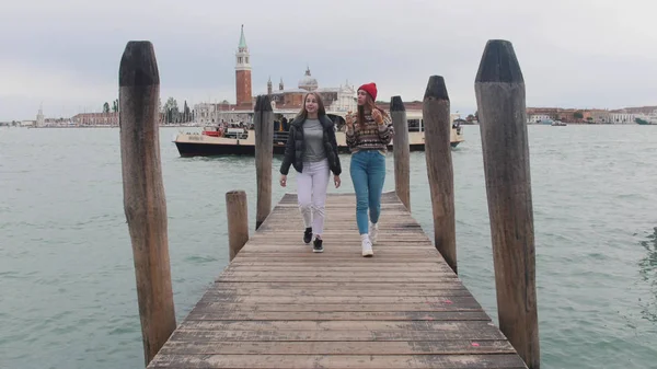 Dos mujeres jóvenes caminando por el muelle. Uno de ellos comiendo helado —  Fotos de Stock