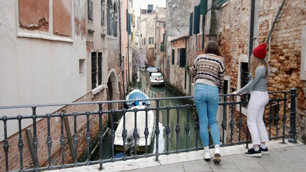 Två unga kvinnor ser långt håll lutande på bron på gatorna i Venedig. — Stockfoto