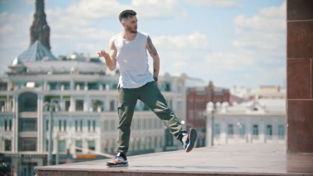 Молодий стильний чоловік танцює на трибуні - центр міста на фоні — стокове відео