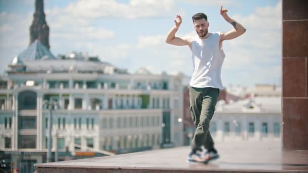 Молодой стильный мужчина с татуировками вольного стиля танцует на стенде - в центре города на заднем плане — стоковое видео