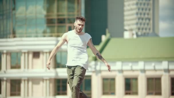 Joven hombre elegante con tatuajes bailando en el estrado y caminando hacia adelante - saltando del estrado - centro de la ciudad en el fondo — Vídeos de Stock