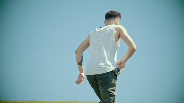 緑のフィールドで踊る白いシャツの入れ墨を持つ若いスタイリッシュな男 — ストック動画