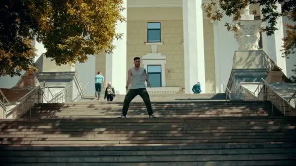 Joven hombre con estilo bailando en las escaleras sobre un fondo de un edificio — Vídeos de Stock