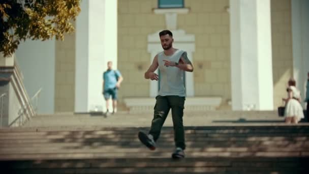 Молодий стильний чоловік з татуюваннями танцює на сходах на фоні будівлі — стокове відео