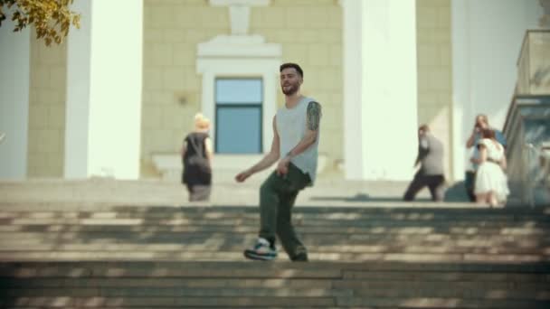 Νέος κομψός χαρούμενος άνθρωπος με τατουάζ χορεύοντας στις σκάλες σε ένα φόντο ενός κτιρίου — Αρχείο Βίντεο