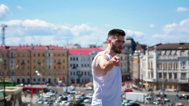 Young attractive man with tattoos freestyle dancing on the top point in the centre of the city - pointing at the camera — Stock Video