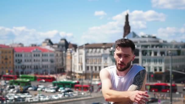 Junger attraktiver stylischer Mann mit Tätowierungen tanzt auf dem obersten Punkt in der Innenstadt - und zeigt in die Kamera — Stockvideo