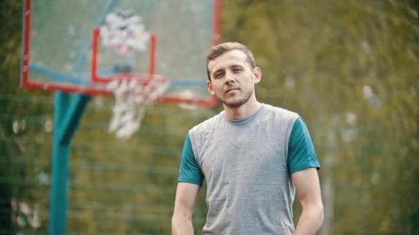 Um homem de pé em um campo de esportes e joga a bola de basquete — Vídeo de Stock