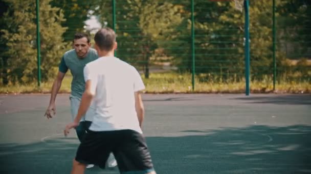 Joven jugando baloncesto en el campo de deportes con amigos, driblando — Vídeo de stock