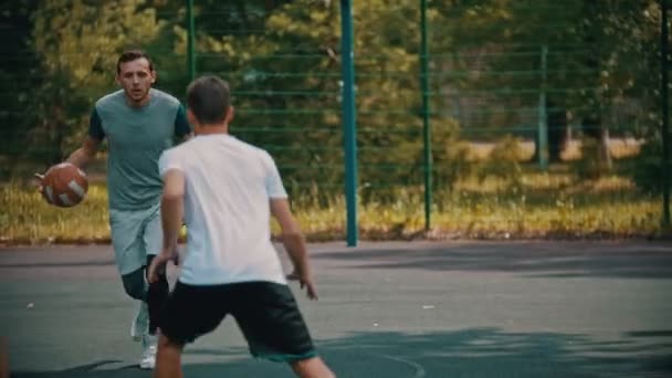 Genç adam arkadaşları ile spor sahasında basketbol oynarken - top sürme, rakiplerinden kaçınarak — Stok video