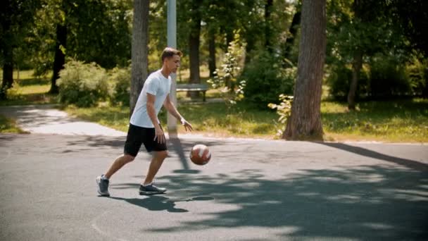 Arkadaşlarıyla spor sahasında basketbol oynayan genç adam - top sürme, rakiplerinden kaçınarak - sepete topu atar — Stok video