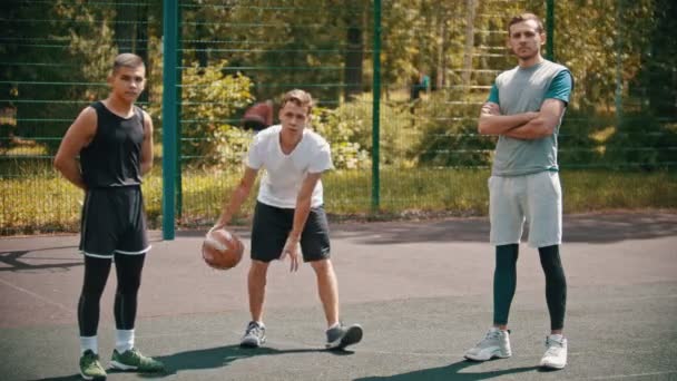 Tři sportováci stojící na hřišti na basketbalu-jeden sportovec udeřil míč ze země — Stock video