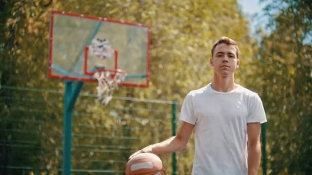 Un joven de pie en un campo de deportes y descarta la pelota del suelo — Vídeos de Stock