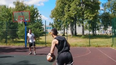 Arkadaşlarıyla dışarıda basketbol oynayan, top sürme ve sepeti eksik genç adam