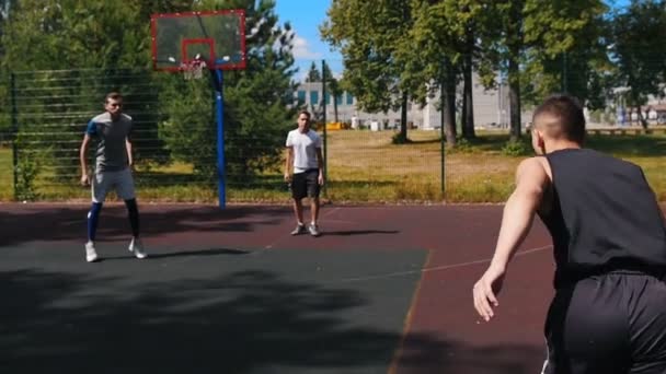 Молодой спортсмен играет в баскетбол на открытом воздухе с друзьями, капает и бросает мяч — стоковое видео