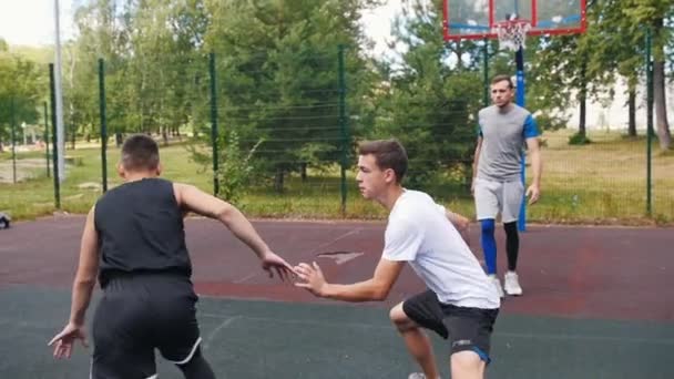 Sportler in schwarzer Uniform spielt draußen Basketball mit Freunden, dribbelt und schießt Tore — Stockvideo