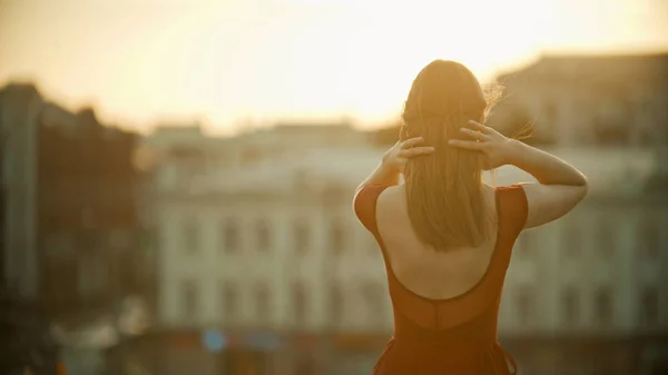 屋根の上に立って、彼女の髪を固定赤いドレスを着た若い女性 - 日没 — ストック写真