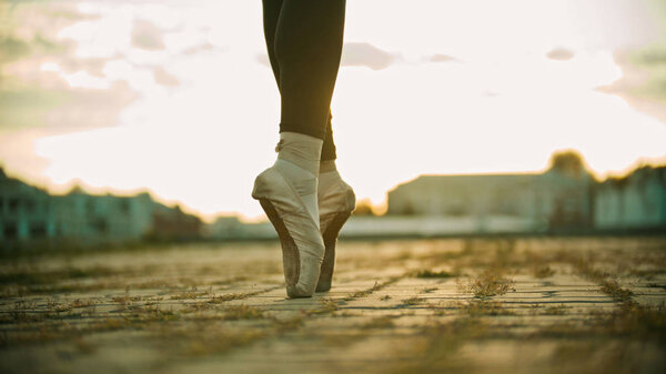 Ноги молодой женщины-балерины, стоящей на крыше на цыпочках - закат
