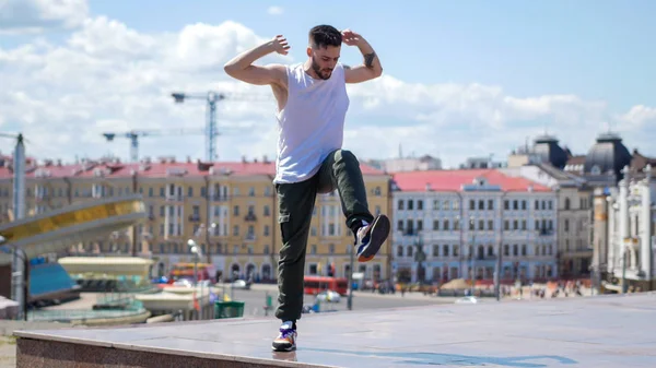 足を上げてスタンドで踊るタトゥーを持つ若い感情的な男 - 背景に街の中心 — ストック写真