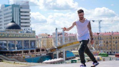 Genç şık adam freestyle dans standında ve arka planda şehrin merkezinde şarkı