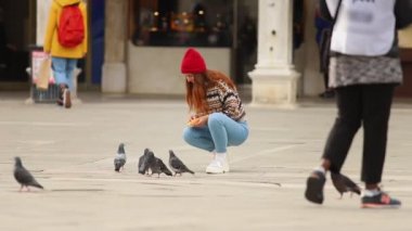 Kasaba meydanında güvercinleri besleyen genç kadın