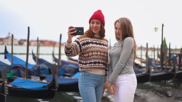Deux jeunes femmes au bord de l'eau avec des bateaux sont photographiées au téléphone et regardent la photo — Video