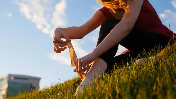 若い女性は彼女の白い尖った靴を履いて、それを結びつける - 日没時に緑の草の上に座って — ストック写真