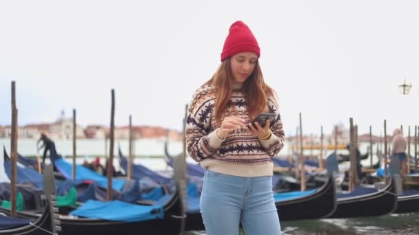 Junge lächelnde attraktive Frau bleibt am Wasser und schaut in ihr Handy — Stockvideo