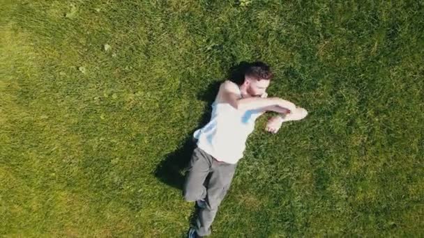 Ένας νέος ελκυστικός άντρας ξαπλωμένος στο γρασίδι χορεύοντας με τα χέρια του — Αρχείο Βίντεο