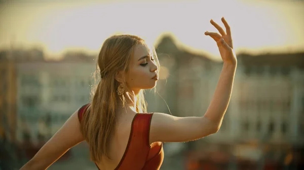 Uma jovem mulher inspirada em vestido vermelho em pé no telhado e graciosamente posando para a câmera - pôr do sol brilhante — Fotografia de Stock