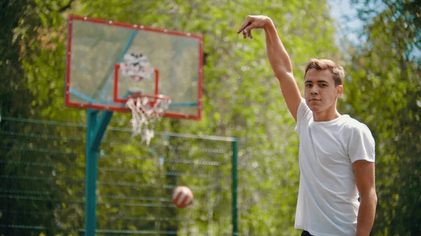 Un joven lanzando la pelota en el aro de baloncesto y se mete en el blanco - un hombre mirando a la cámara — Foto de Stock