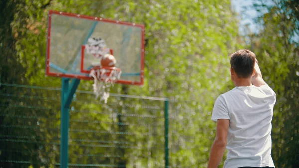 Ein junger Mann wirft den Ball in den Basketballkorb und dieser landet im Ziel — Stockfoto