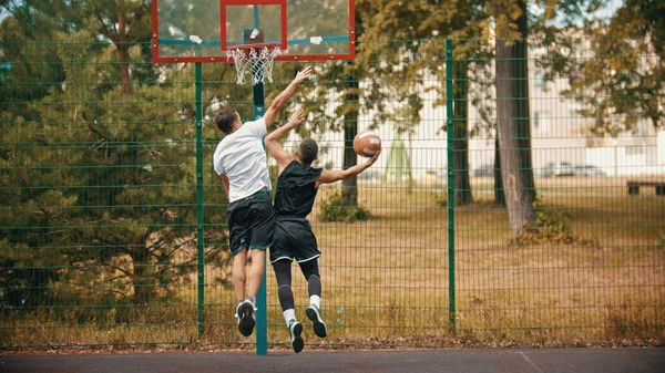 Jovens homens jogando basquete no campo de esportes ao ar livre protegendo o aro de basquete do ataque — Fotografia de Stock