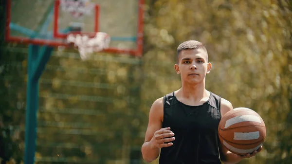 Ein junger, athletischer Mann steht auf einem Sportplatz und hält einen Basketballball — Stockfoto