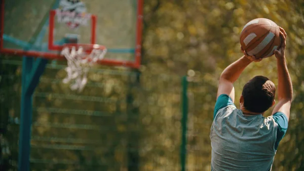 若い男がジャンプし、バスケットボールのフープでボールを投げようとしている — ストック写真