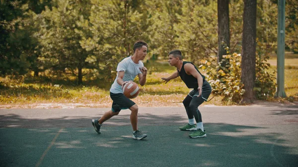 Jeunes hommes jouant au basket sur le terrain de sport à l'extérieur un homme dribble évitant son adversaire — Photo